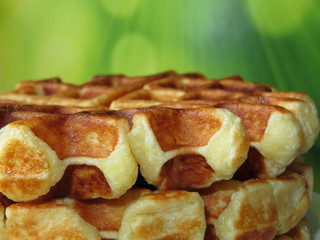 Stack of Belgian waffles on a green background. Tasty breakfast, homemade wafer