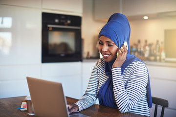 Smiling Arabic entrepreneur talking on a phone in her kitchen