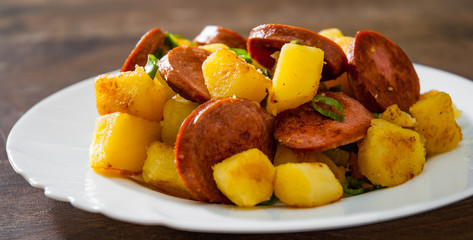 Roasted Potato and Sausage in white plate on wooden table