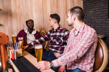Cheerful old multiracial friends having fun and drinking draft beer at bar counter in pub.