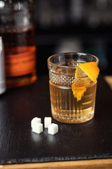 Glass of  whiskey (cognac or brandy) with lemon and ice cubes standing on the bar counter with a bottle on the background