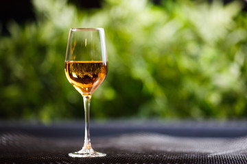 A glass of white wine or apple juice stands on a table in good light with a beautiful green background.