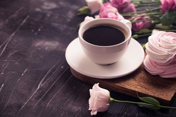 Coffee cup, lisianthus flower and raspberry meringue on dark desk. 