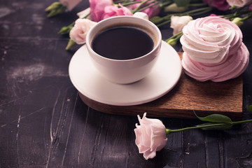 Coffee cup, lisianthus flower and raspberry meringue on dark desk. 