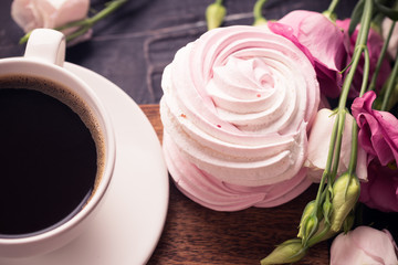 Coffee cup, lisianthus flower and raspberry meringue on dark desk. 