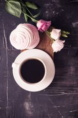 Coffee cup, lisianthus flower and raspberry meringue on dark desk. 