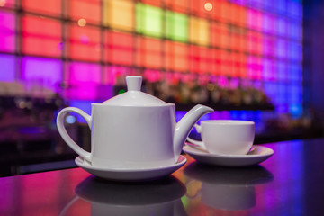 White teapot and tea cup on color lights background
