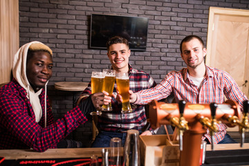 Handsome men's are clinking glasses of beer and smiling while resting in pub