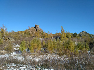 The autumn landscape with the high rock, yellow trees and show on the sunny day.