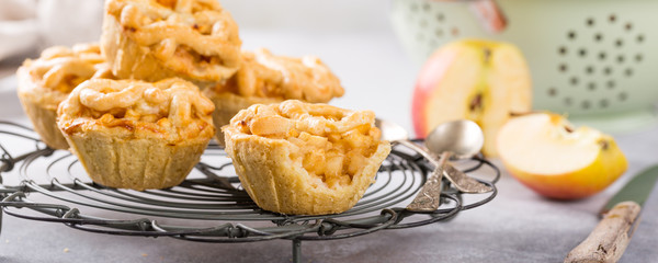 Homemade mini apple pies on metal rack on light concrete background. Healthy food concept. Banner.