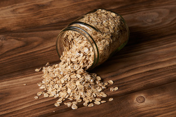 Oatmeal glass jar on wooden background. Glass jar with oatmeal flakes, close-up. Scattered oat. Dry, uncooked oat flakes, oatmeal in glass transparent jar, Healthy food and agriculture concept