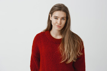 Girl expresses disdain to rival. Portrait of displeased unimpressed beautiful woman in fashionable red loose sweater, smirking from contempt, doubting if she could trust person over gray background