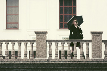 Young fashion woman in black coat with umbrella walking in city street