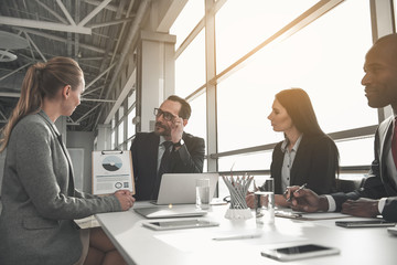Colleagues sitting together around office desk and looking at chart with interest