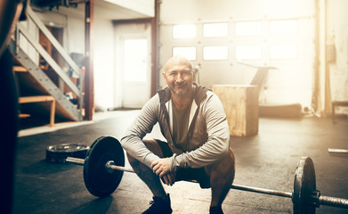 Smiling mature man crouching by weights in a gym