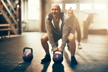 Smiling mature man lifting dumbbells during a gym exercise class