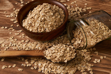 Oat flakes oatmeal in bowl and wooden spoon on wood table background. Healthy vegetarian diet food and agriculture concept