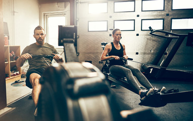 Two fit people working out on gym rowing machines