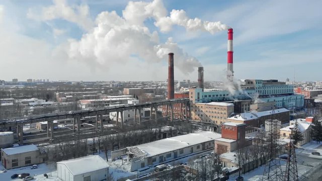 Dense thick smoke coming from industrial red-white pipes. Smooth aerial shooting of a power plant from a bird's eye view. Industrial environmental pollution with the fume.