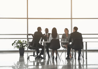 Group of colleagues resting on office chairs in boardroom near big window. One of the men straightening his tie