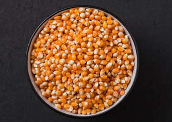 Black bowl with raw sweet corn and popcorn on wood