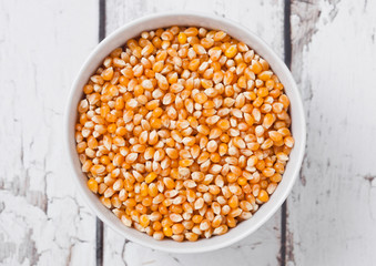 White bowl with raw sweet corn and popcorn on wood