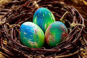 Three multi-colored Easter eggs lie in a nest of dark branches