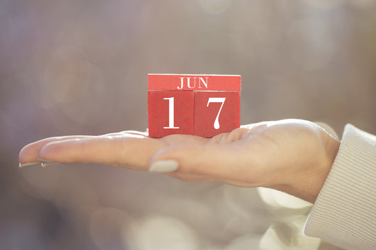 the woman is holding a red wooden calendar. Red wooden cube shape calendar for JUN 17 with hand 