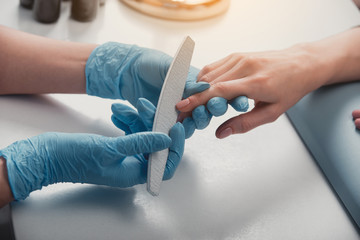 Close up female master arm polishing fingernails with nail file. They locating at desk