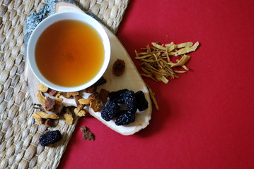 Bowl of chinese herb tea with pieces of astragalus and huang qi roots and jujubes on red background. Top view.