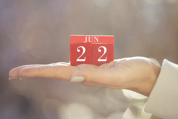 the woman is holding a red wooden calendar. Red wooden cube shape calendar for JUNE 22 with hand 