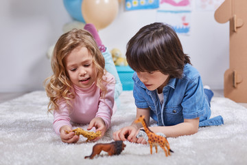 Portrait of joyful girl and boy toying with statuette of wild animals. Kids examining figures with interest. Fantasy concept