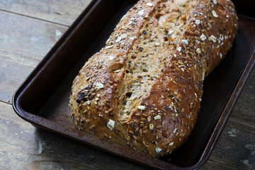 Rustic whole grain bread loaf in baking tray on wooden table