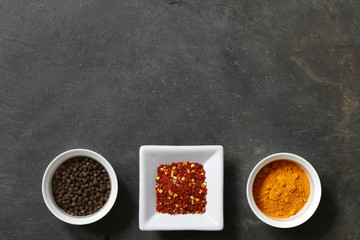 Various spices with peppercorn, cumin, hot peppers and turmeric on slate background with copy space