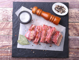 Raw fresh meat, uncooked lamb or beef ribs with pepper, garlic, salt, bay leaves and spices on dark stone background, Ready for cooking. copy space.