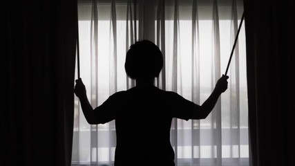 Backlit woman close curtains in the city.