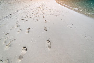 Footprints on the white beach with a blue and green wave. Summer holidays activity concept. Copy space.