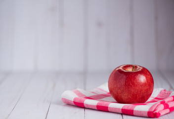 A single apple on a whitewashed wood top with a vintage red check dish towel.