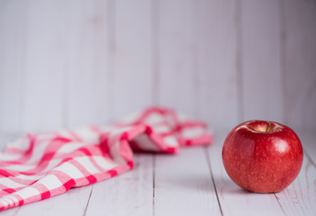 A single apple on a whitewashed wood top with a vintage red check dish towel.