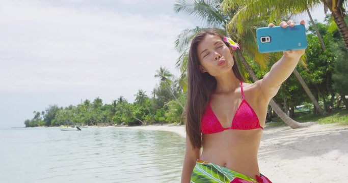 Woman taking smart phone selfie video or photo- Bikini travel girl on beach smiling happy on Paradise Beach. Joyful girl on holidays beach vacation wearing bikini. RED EPIC SLOW MOTION.