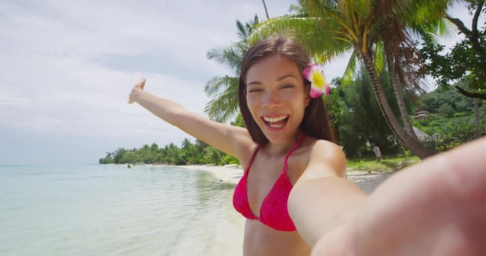 Selfie video - Bikini travel woman on beach smiling happy on a motu Beach, Bora Bora. Happy joyful girl on holidays beach vacation wearing bikini and frangipani hair flower in Tahiti, French Polynesia
