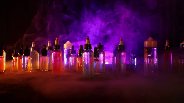 Vape concept. Slider shot. Smoke clouds and vape liquid bottles on dark background. Light effects. Useful as background or vape advertisement. Selective focus