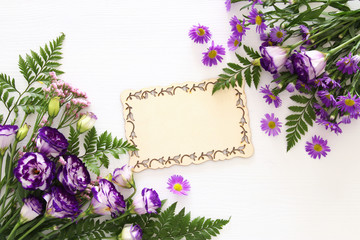 Top view of purple beautiful flowers arrangement and wooden board over white background. Copy space.