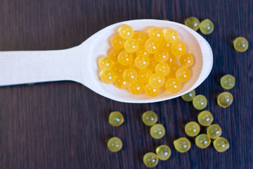 Fish oil. Cod liver oil omega 3 gel capsules. Granules in wooden spoon on dark background