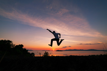 Asian man traveler is jumping on top of a rainforest mountain in scenery sunrise or sunset time background.