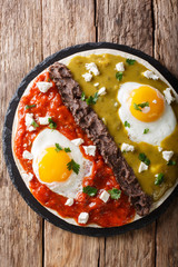 Mexican fried huevos divorciados eggs with salsa verde and roja, cheese, black beans on a tortilla close-up. Vertical top view