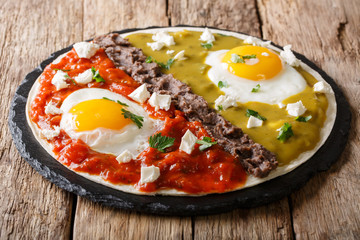 Mexican fried huevos divorciados eggs with salsa verde and roja, cheese, black beans on a tortilla close-up. horizontal