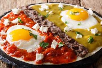 Delicious mexican dish: eggs huevos divorciados with Frijoles refritos, sauces roja and verde and cheese Queso Fresco on a corn tortilla macro. Horzontal