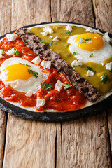 Mexican breakfast: eggs huevos divorciados with beans Frijoles refritos, two sauces roja and verde and cheese Queso Fresco close-up. Vertical