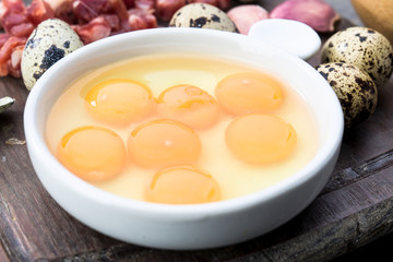 raw and open quail eggs in porcelain bowl, on rustic wood